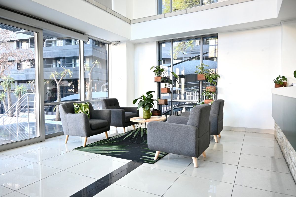 Bright and modern commercial entrance lobby featuring double volume ceilings, large floor-to-ceiling windows, and polished tile flooring.