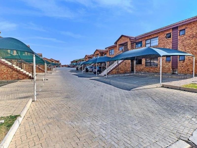 Exterior view of a residential complex featuring face brick buildings, paved driveway areas, and dedicated shade cloth carports for residents.