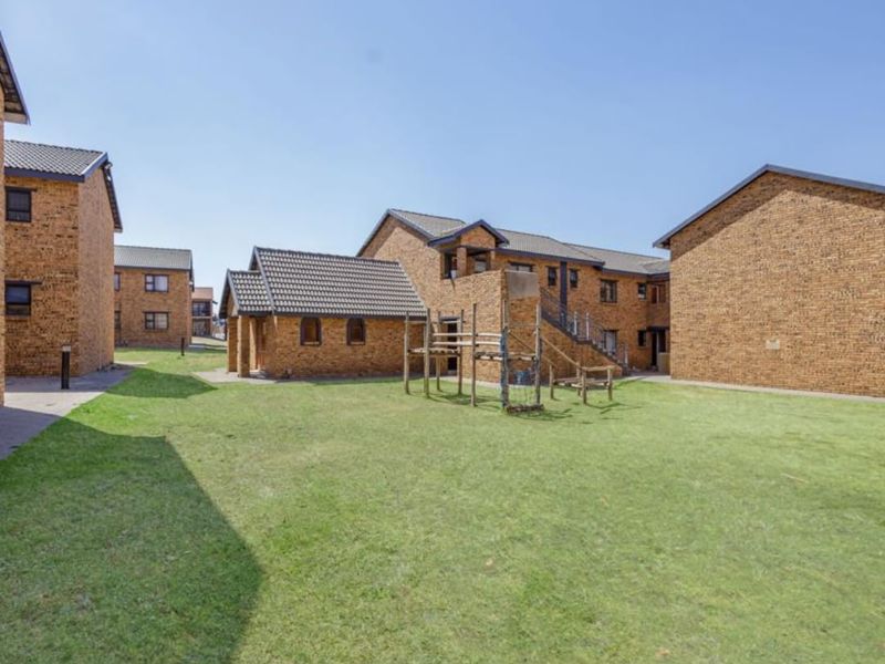 A view of the communal garden area between face brick residential buildings, featuring paved walkways and established lawn.