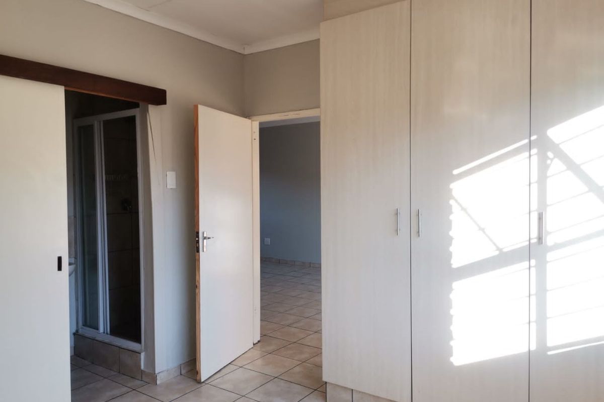A bright, empty bedroom featuring built-in cupboards, tiled flooring, and an en-suite shower room.