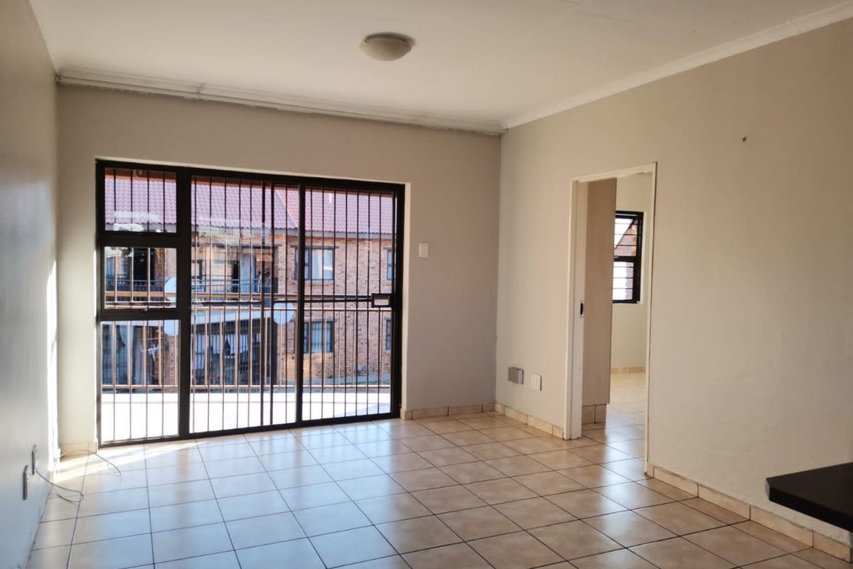 An empty living room featuring tiled flooring and a large sliding glass door with integrated security bars, providing access to an exterior balcony area.