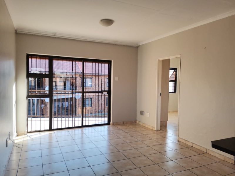 An empty living room featuring tiled flooring and a large sliding glass door with integrated security bars, providing access to an exterior balcony area.