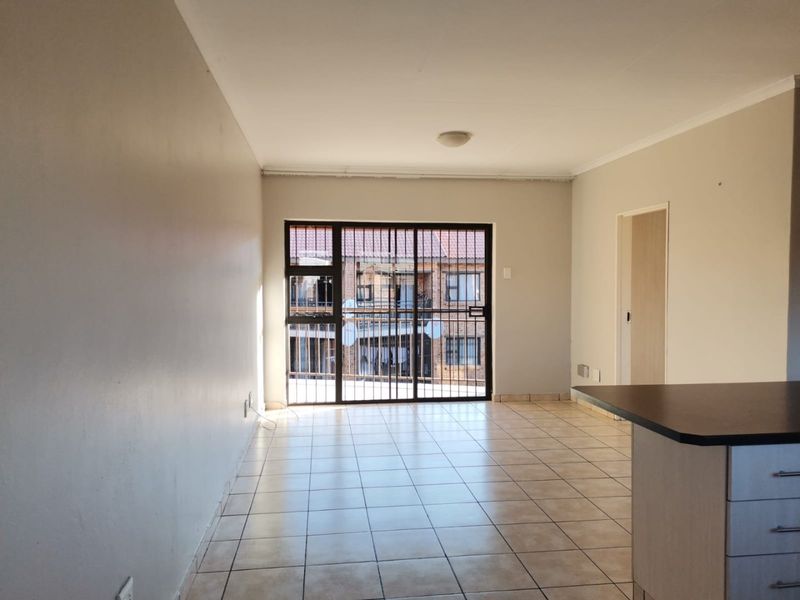 An open-plan living area featuring tiled flooring, a kitchen counter, and a sliding door with a security gate leading to an exterior balcony.