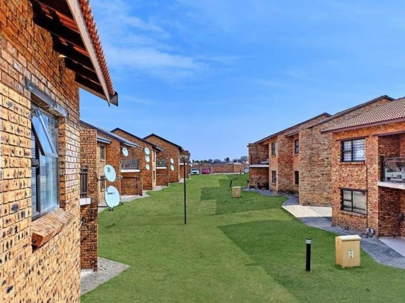 A view of a residential complex featuring face brick buildings, tiled roofs, and a well-maintained communal lawn area between the units.