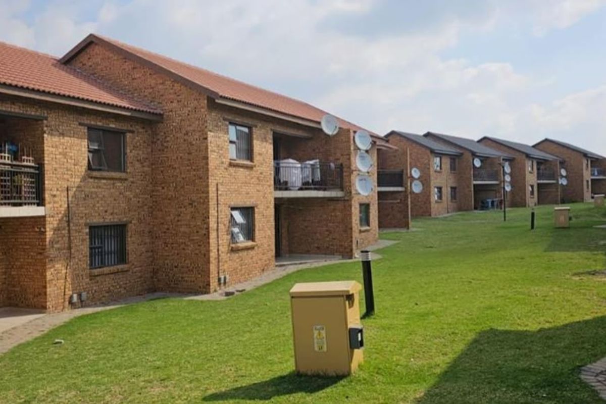 Exterior view of a multi-unit residential complex featuring face brick construction, tiled roofs, and shared green spaces with paved pathways.