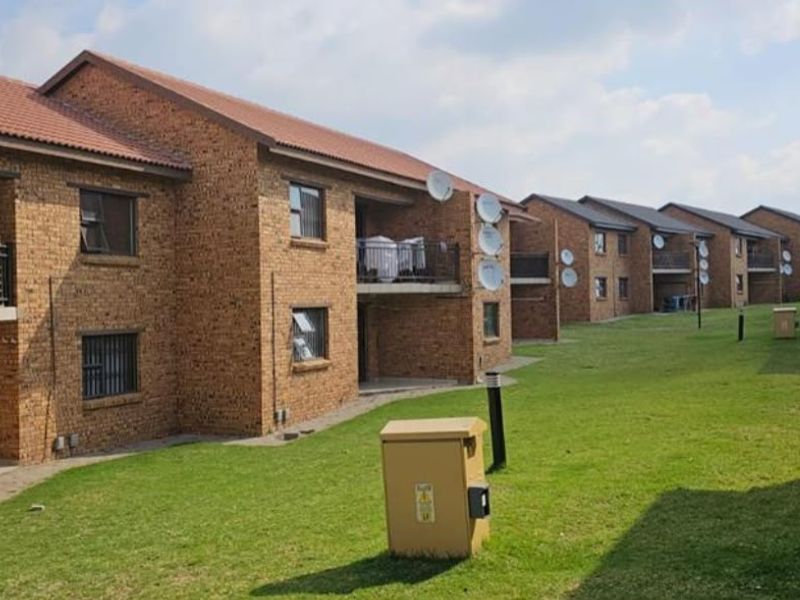 Exterior view of a multi-unit residential complex featuring face brick construction, tiled roofs, and shared green spaces with paved pathways.