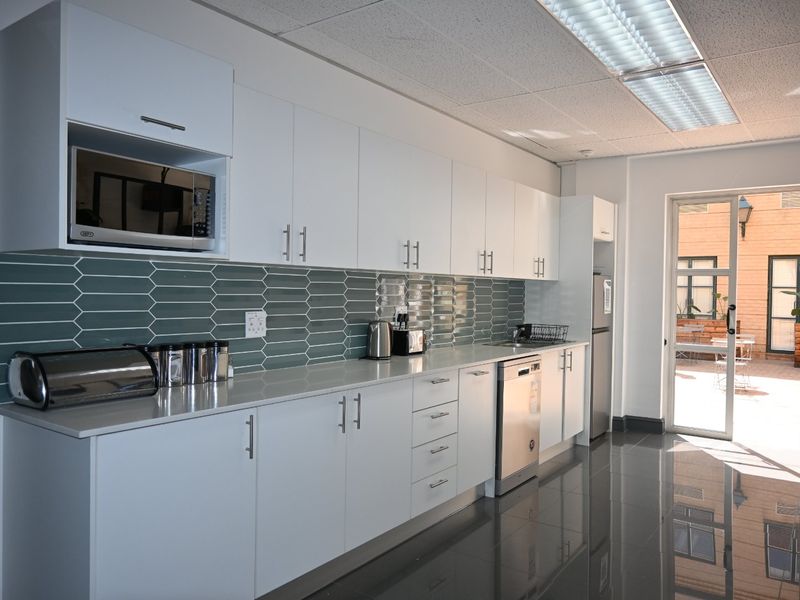 Modern commercial kitchen featuring white cabinetry, sleek tiled backsplash, integrated appliances, and polished dark floor tiles with direct access to an outdoor area.