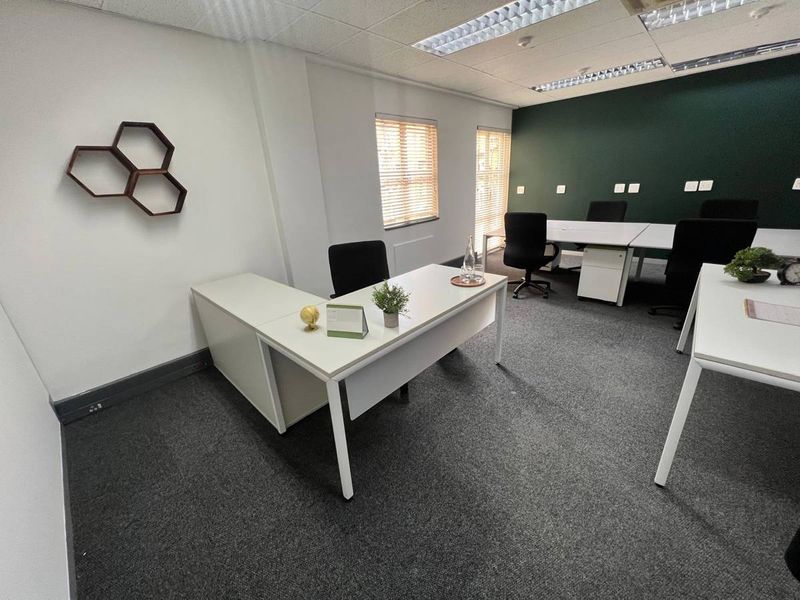 A well-maintained commercial office space featuring carpeted flooring, suspended ceilings with recessed lighting, and large windows with venetian blinds.
