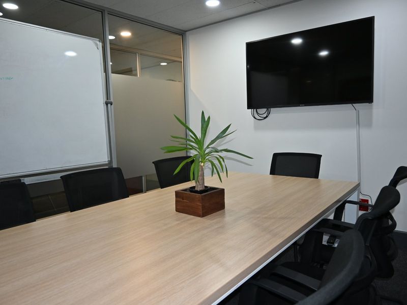 A professional meeting room featuring a glass partition wall, recessed lighting, and a wall-mounted television for presentations.