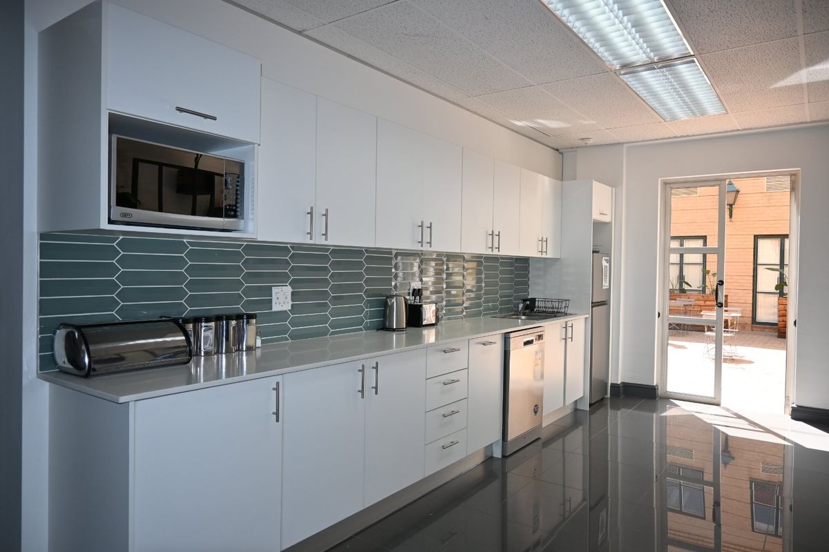 Modern commercial kitchen featuring white cabinetry, sleek tiled backsplash, integrated appliances, and polished dark floor tiles with direct access to an outdoor area.