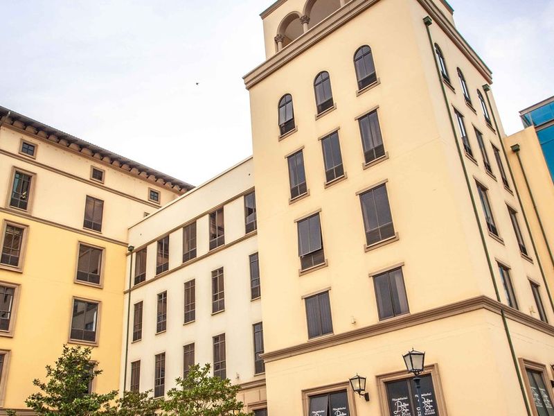A modern commercial building featuring a mix of traditional architectural elements, arched windows, and a prominent glass-enclosed elevator or stairwell section.
