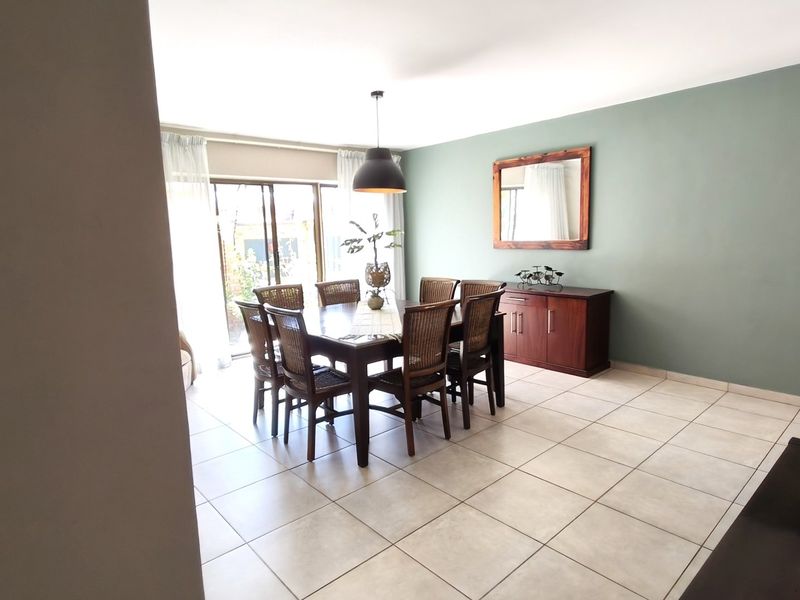 A bright dining room featuring neutral tiled flooring, a modern pendant light, and large sliding glass doors providing access to the outdoor area.