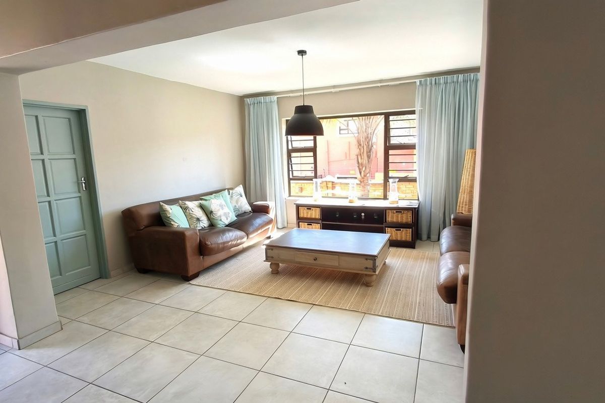 A bright and spacious living room featuring neutral tiled flooring, a large window allowing natural light, and a modern pendant light fixture.