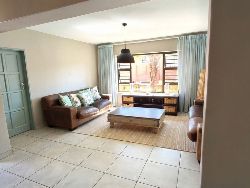 A bright and spacious living room featuring neutral tiled flooring, a large window allowing natural light, and a modern pendant light fixture.