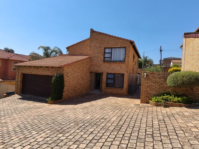 A well-maintained double-storey face-brick house featuring a paved driveway, integrated double garage, and secure boundary walling.