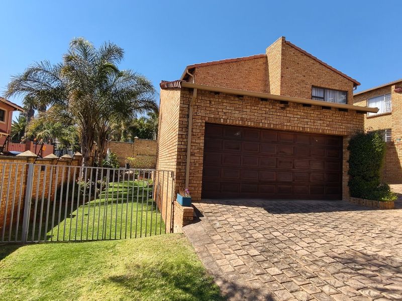 Front view of a face-brick residential property featuring a paved driveway, double garage, and a fenced garden area.