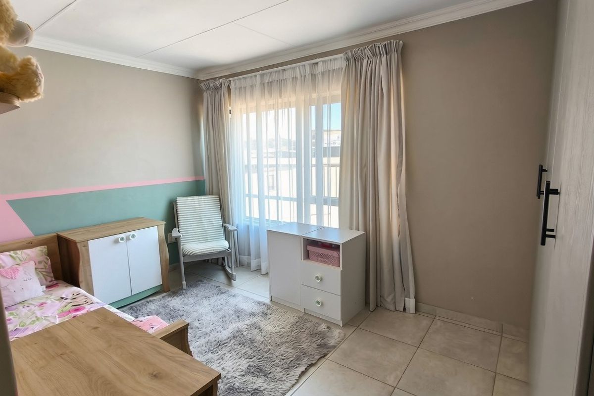 A well-maintained bedroom featuring tiled flooring, built-in cupboards, and large windows with curtain rails, offering a bright and functional living space.