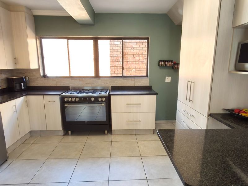 Modern kitchen featuring light wood cabinetry, dark granite countertops, a gas stove with oven, and tiled flooring with a neutral backsplash.