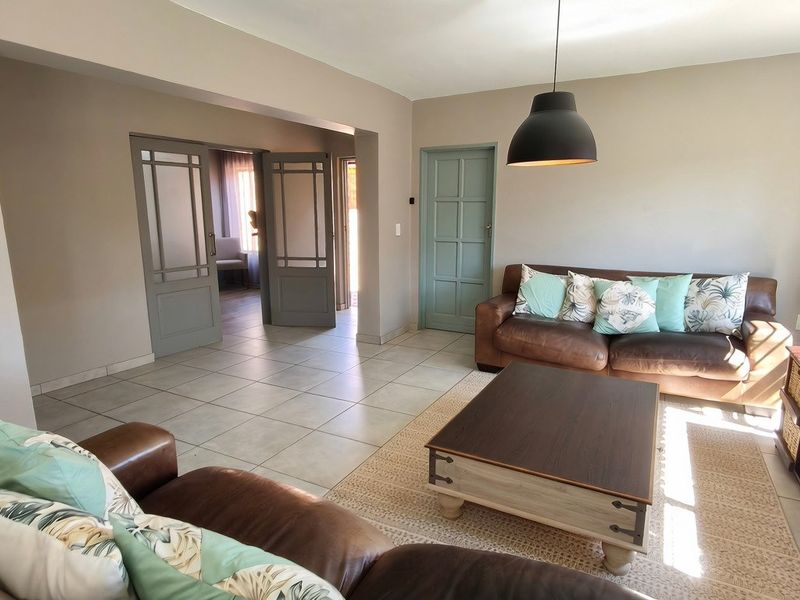 A bright and spacious living room featuring neutral tiled flooring, modern pendant lighting, and classic panelled interior doors leading to adjacent living spaces.