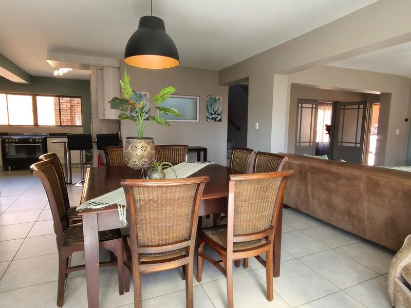 Spacious open-plan living and dining area featuring tiled floors, modern pendant lighting, and a functional kitchen with built-in appliances.