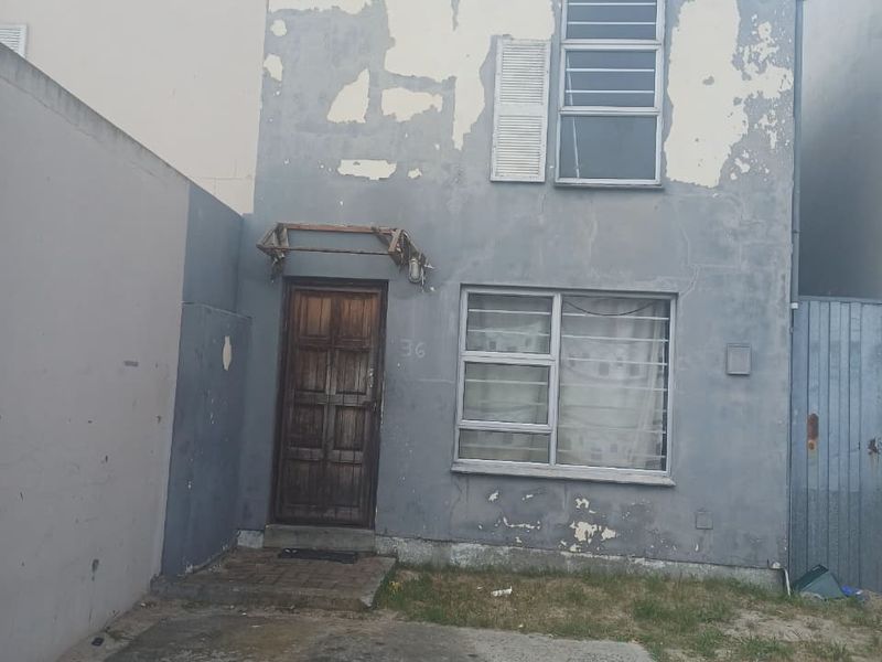 Front elevation of a two-story house featuring a concrete driveway, timber entrance door, and aluminium windows, currently requiring significant exterior maintenance and repainting.