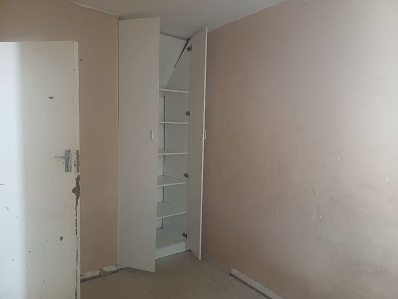 An empty bedroom featuring a built-in cupboard, tiled flooring, and walls in need of cosmetic attention.