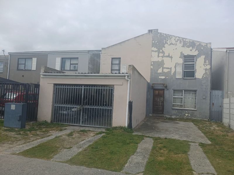 Front elevation of a two-story residential property featuring a garage, driveway, and weathered exterior facade requiring maintenance.