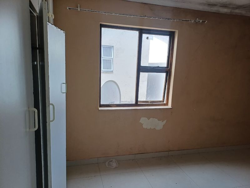 An empty bedroom featuring built-in cupboards and tiled flooring, requiring cosmetic updates to the walls and ceiling to restore its condition.