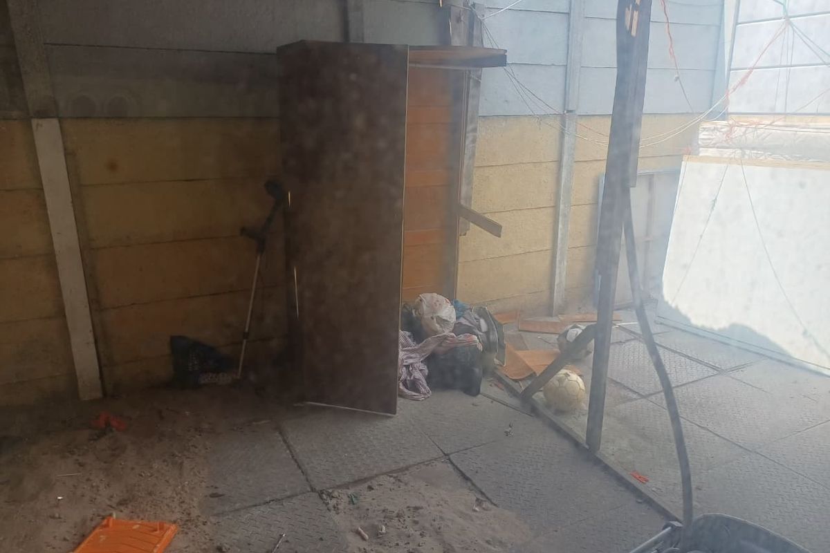A neglected rear outdoor area featuring precast concrete walling and paved flooring, currently showing significant signs of wear and accumulation of debris.
