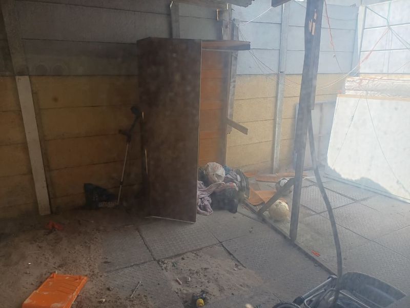 A neglected rear outdoor area featuring precast concrete walling and paved flooring, currently showing significant signs of wear and accumulation of debris.
