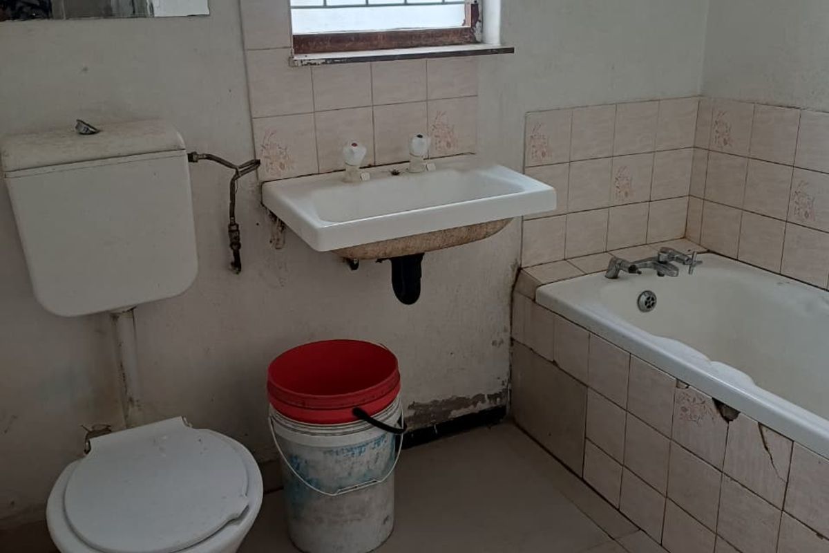 A dated bathroom featuring a built-in bathtub, wall-mounted basin, and flush toilet, requiring significant renovation and cosmetic updates to improve its condition.