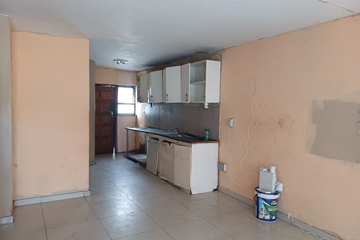A dated, empty kitchen area featuring basic built-in cabinetry, a stainless steel sink, and tiled flooring, requiring cosmetic updates and renovation.