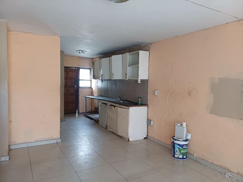 A dated, empty kitchen area featuring basic built-in cabinetry, a stainless steel sink, and tiled flooring, requiring cosmetic updates and renovation.