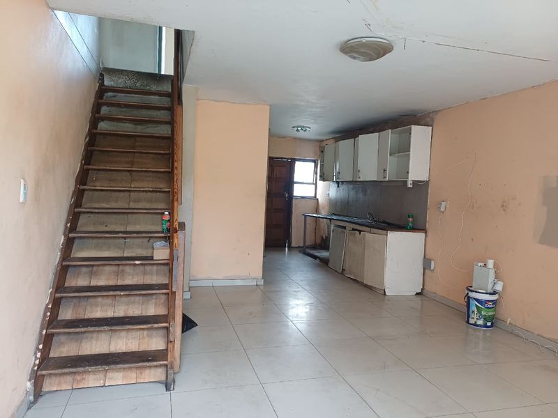 Open plan living area featuring a staircase and basic kitchen cabinetry, requiring significant renovation and cosmetic updates to restore functionality and appeal.