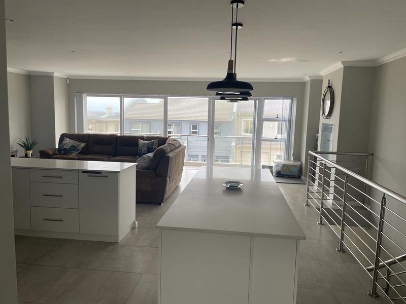 Spacious open-plan living area featuring a modern kitchen island with stone countertops, tiled flooring, and large sliding doors leading to a balcony.