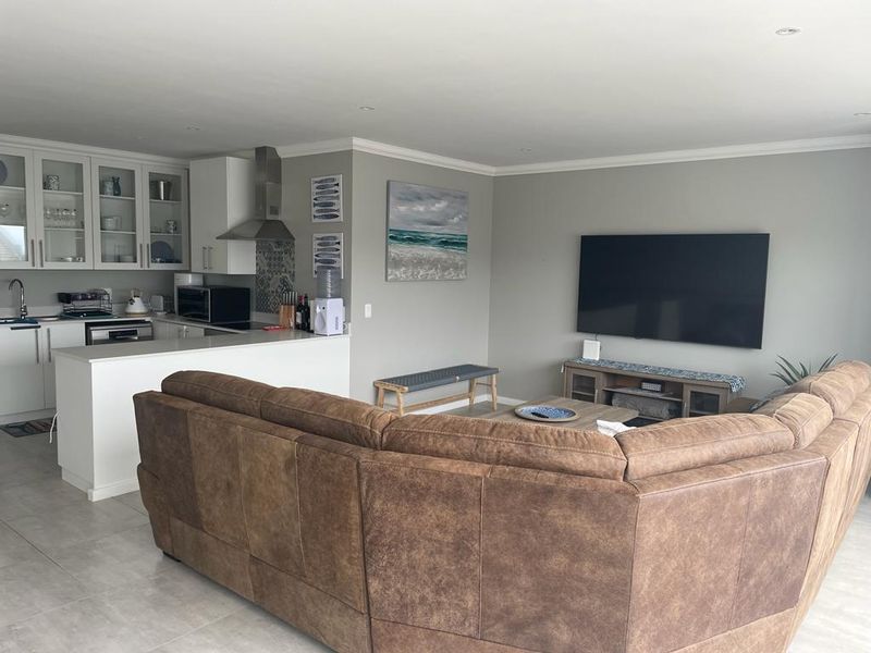 A bright open-plan living and kitchen area featuring modern cabinetry, stone countertops, stainless steel extractor, and neutral tiled flooring throughout.