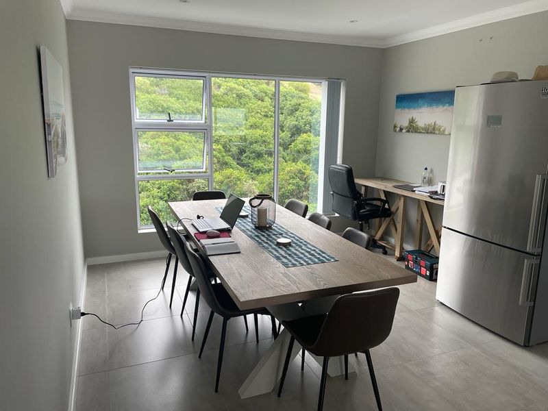 A bright open-plan living and dining area featuring large windows with natural views, neutral wall tones, and modern tiled flooring throughout.