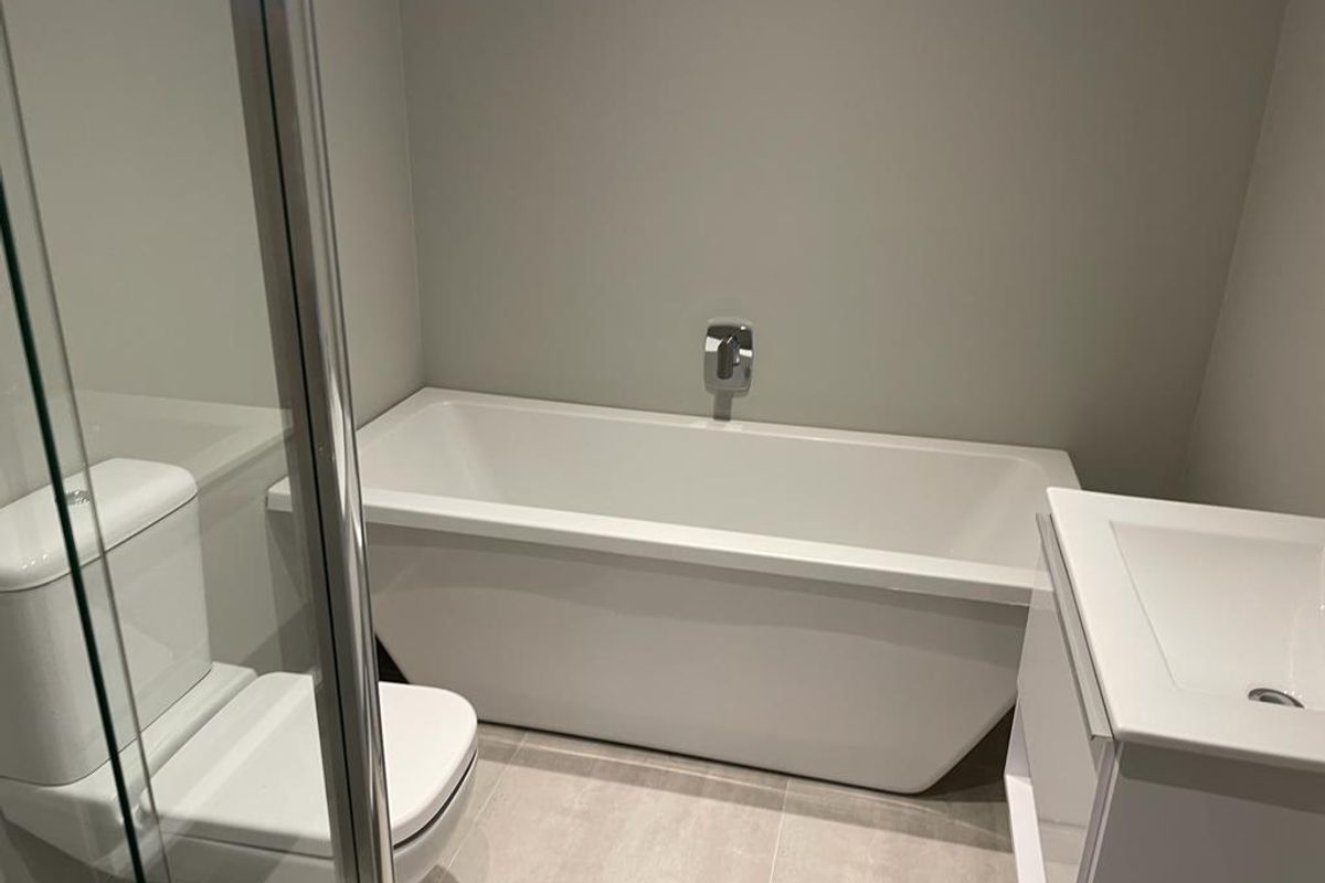 Modern bathroom featuring a sleek freestanding bathtub, wall-mounted mixer, vanity unit with basin, toilet, and a glass-enclosed shower with neutral tiled flooring.