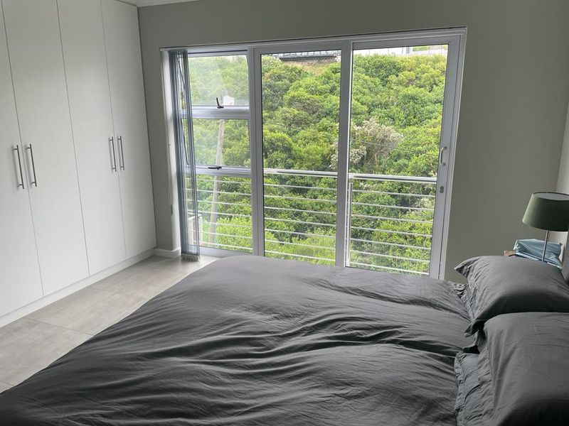 Modern bedroom featuring built-in cupboards, tiled flooring, and a large sliding glass door opening to a balcony with scenic greenery views.
