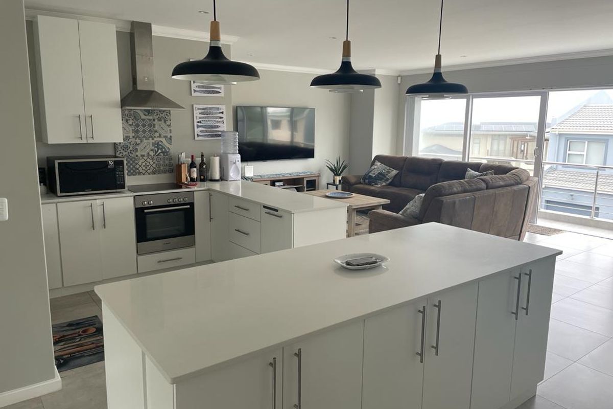 Modern open-plan living area featuring a contemporary kitchen with a central island, built-in appliances, and seamless flow to an outdoor balcony.