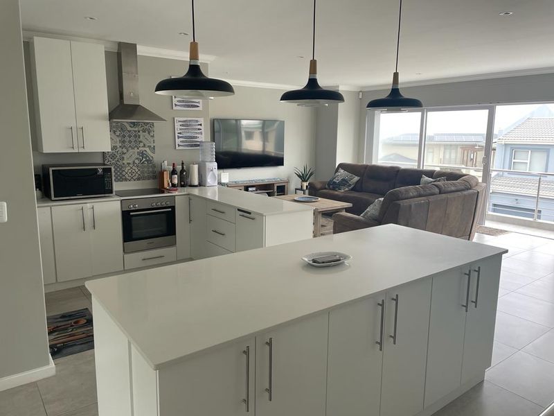 Modern open-plan living area featuring a contemporary kitchen with a central island, built-in appliances, and seamless flow to an outdoor balcony.
