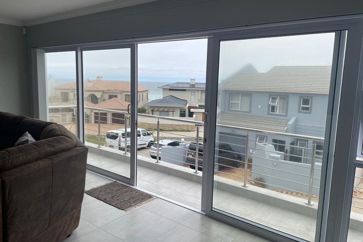 Spacious living area featuring large sliding glass doors that open onto a balcony with stainless steel railings and coastal neighborhood views.