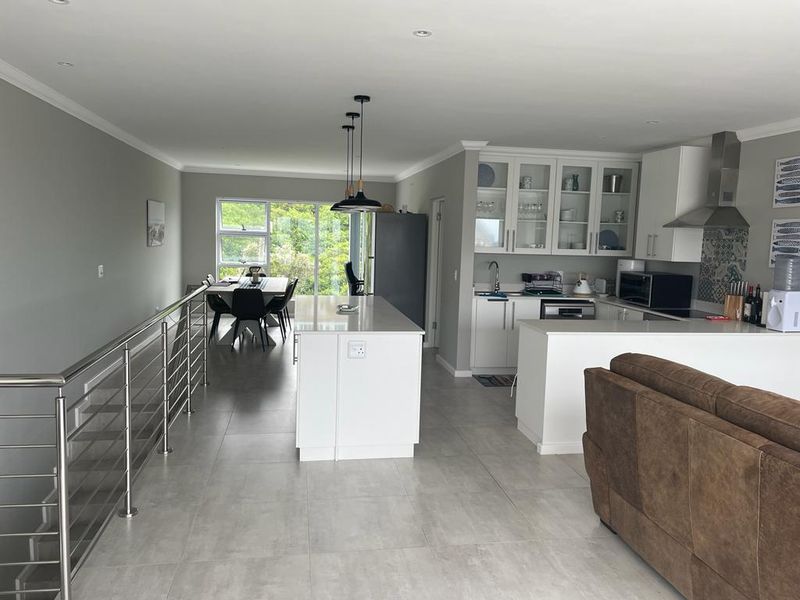 Spacious open-plan living area featuring a modern kitchen with a central island, sleek cabinetry, and a stainless steel balustrade overlooking the lower level.