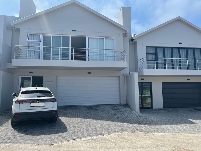Modern double-story residential facade featuring a paved driveway, double garage, and upper-level balconies with stainless steel balustrades.