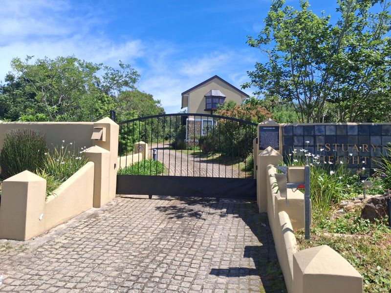 Front entrance view of Estuary Heights featuring a paved driveway, secure wrought iron gate, and established boundary wall with signage.