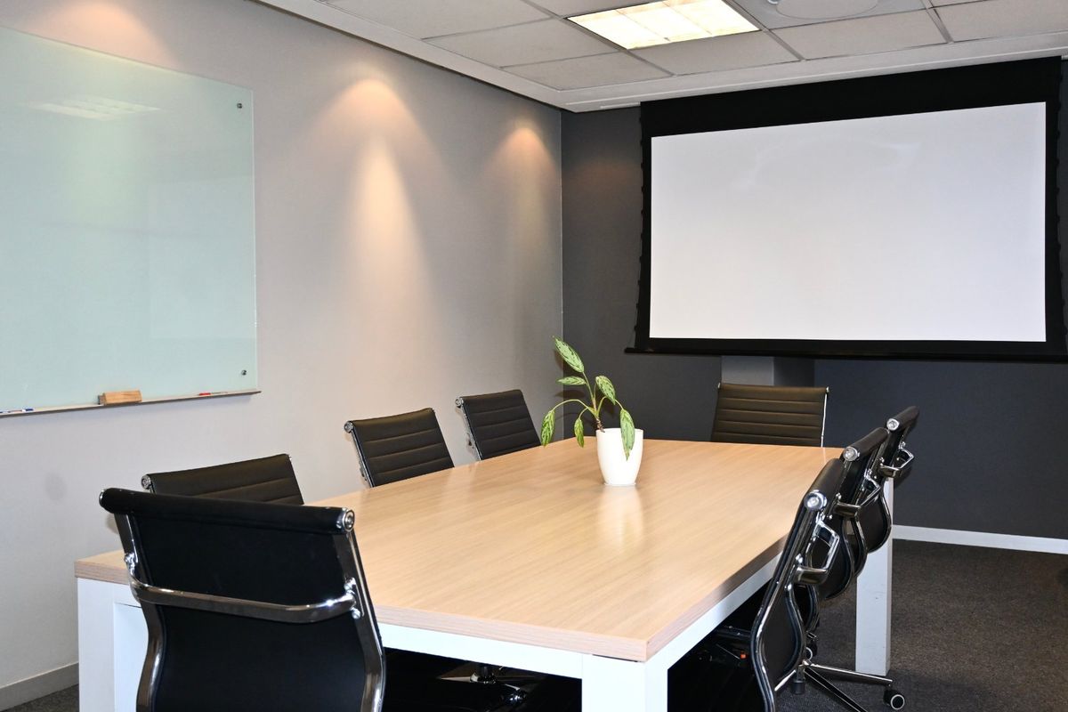 A professional meeting room featuring a wall-mounted glass whiteboard, a retractable projector screen, and recessed ceiling lighting.