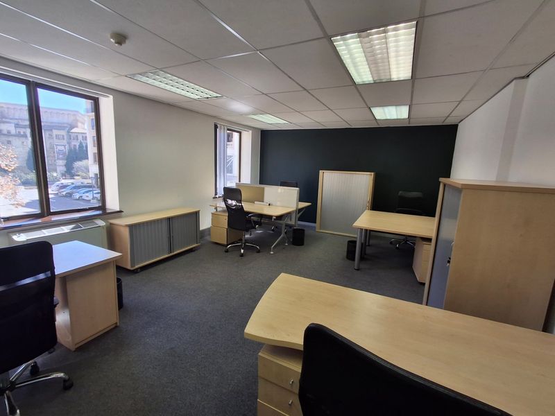 A functional commercial office space featuring suspended ceilings, recessed lighting, carpeted flooring, and large windows providing natural light.