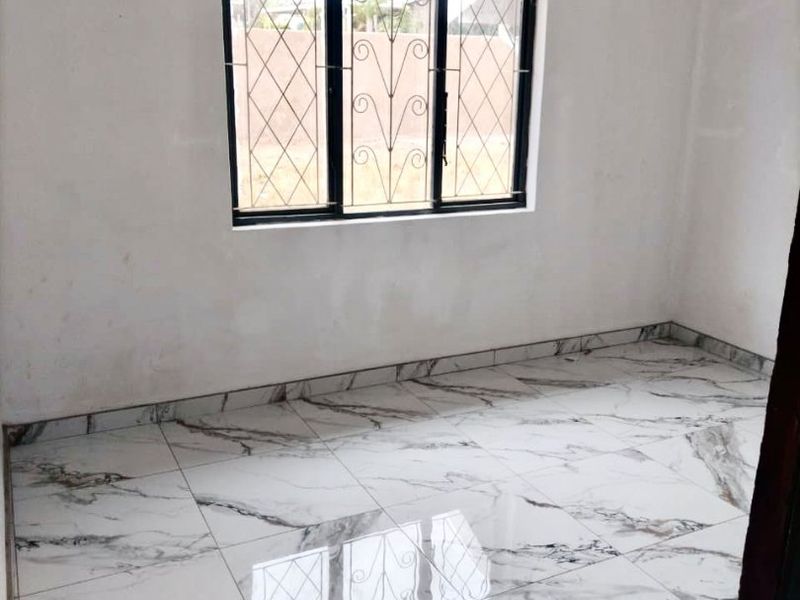 A bright, empty bedroom featuring modern marble-look floor tiles and a window fitted with security burglar bars.