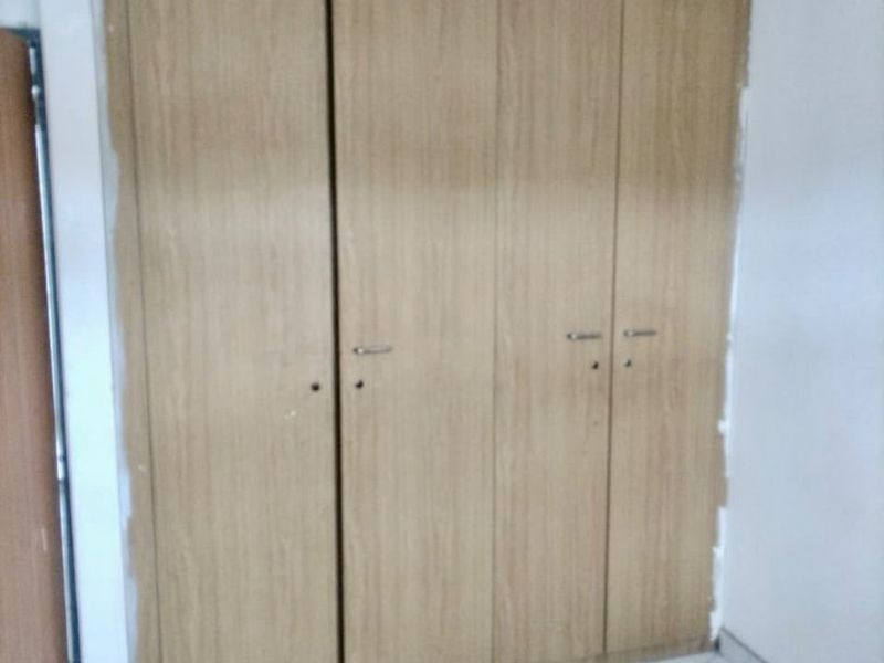 A bedroom featuring a built-in wooden wardrobe and marble-effect tiled flooring, currently requiring minor finishing touches to the surrounding wall paint.