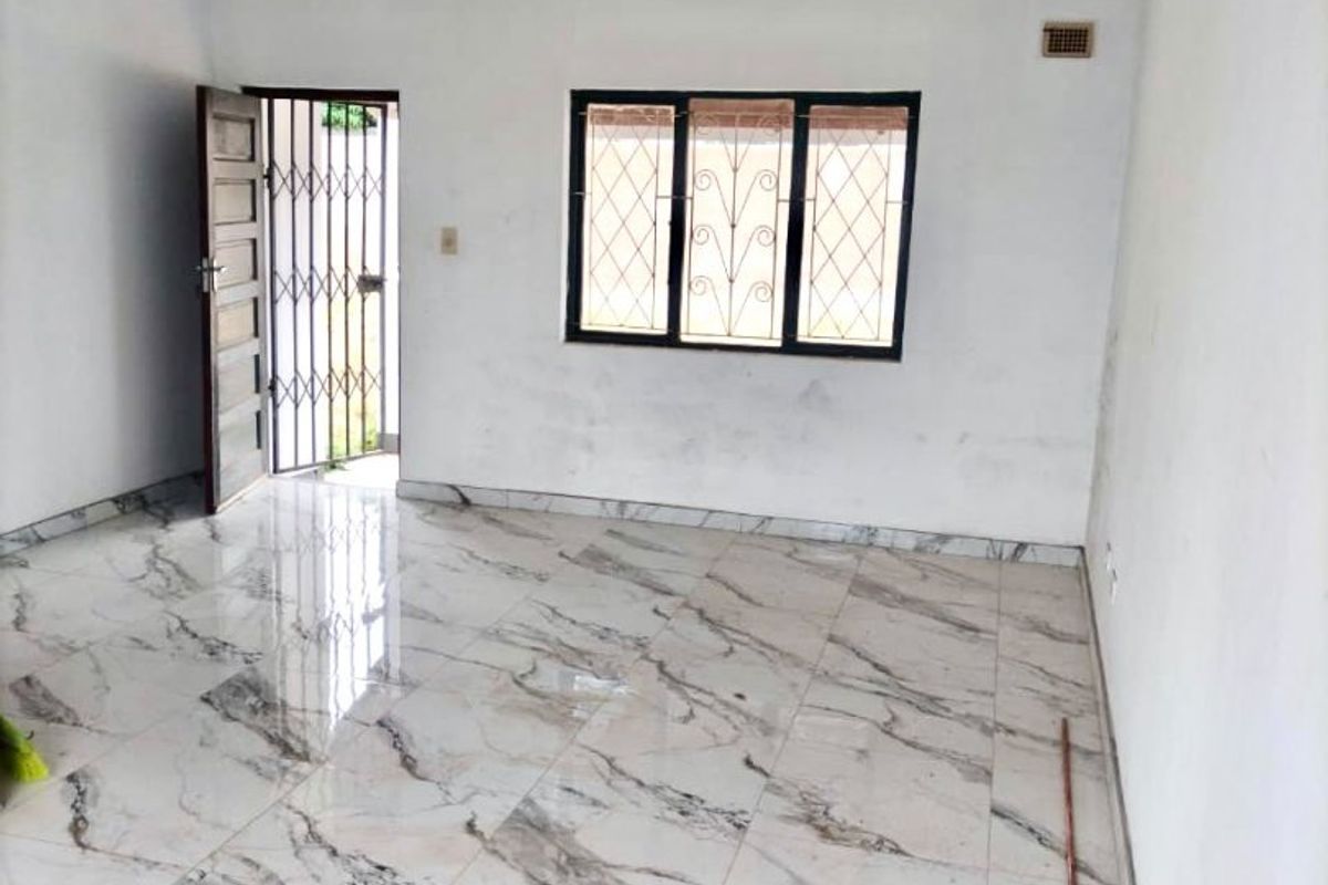 An empty living room featuring polished marble-look floor tiles, a security gate, and a window with security bars.